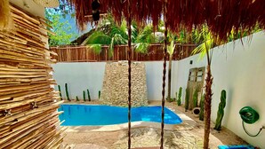 A swimming pool with a swing, surrounded by a stone wall, palm trees, and a thatched roof. - Awesome jungle villa with pool La Veleta (Tulum)