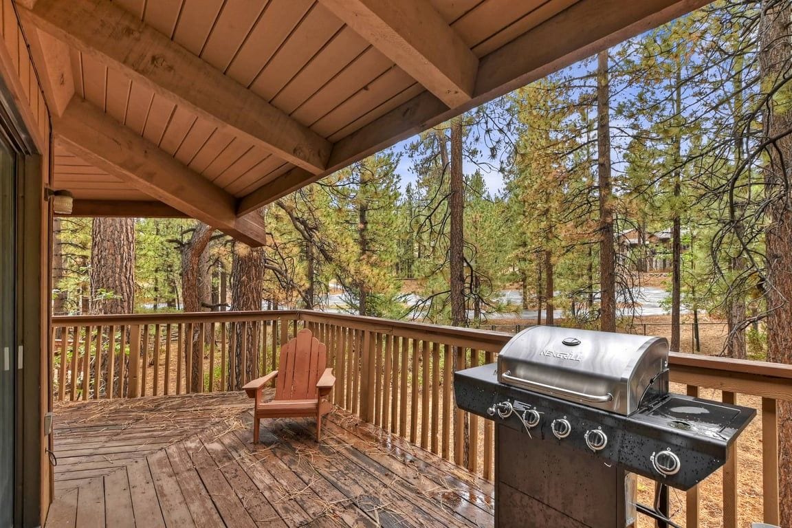 A wooden deck with a grill and a chair, surrounded by trees.