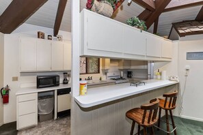 A kitchen with white cabinets, a microwave, a stove, and a sink. There are two wooden chairs at the counter.