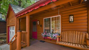 Een houten hut met een veranda, een rode deur en een bankje.