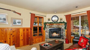 A cozy living room with a fireplace, wooden furniture, and a view of the outdoors. - Stepping Back in Time by Destination Big Bear : Nestled in Moonridge Close to Both Resorts, Hiking & Biking Trails! (Big Bear Lake)