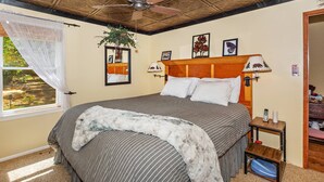 Een slaapkamer met een bed, een plafondventilator, een raam met uitzicht en een nachtkastje met een lamp.