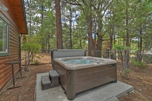 Un jacuzzi en un área boscosa con una cabaña de madera cerca.