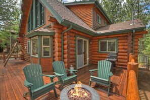 A log cabin with a deck, two Adirondack chairs, a fire pit, and a grill.