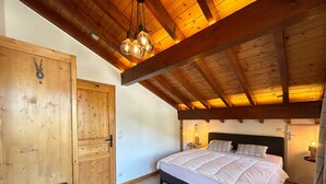 Un dormitorio con techo de madera, una cama con ropa de cama blanca, una mesita de noche y una puerta.