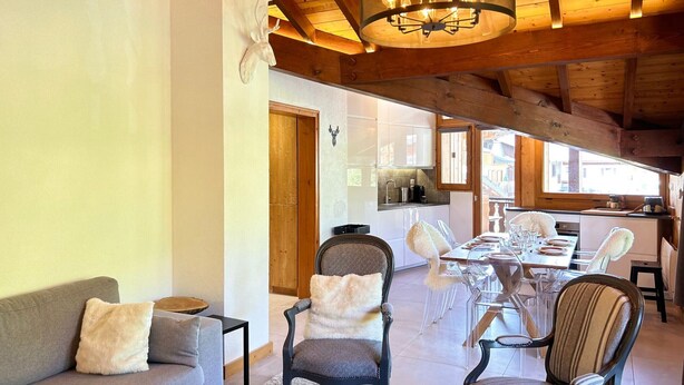 Un interior acogedor con techo de madera, un comedor con mesa y sillas, y una cocina visible a través de un umbral abierto.