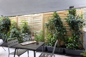 Eine Terrasse mit Tisch und Stühlen, umgeben von üppiger Bepflanzung und einem Holzzaun.
