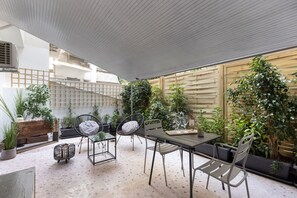 Ein Patio mit Tisch und Stühlen, umgeben von Blumentöpfen und einem Holzzaun.