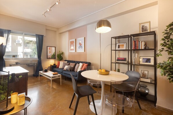 Ein modernes Wohnzimmer mit Sofa, Couchtisch und Esstisch. Bücherregale und ein Blumentopf sind ebenfalls vorhanden.