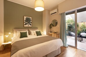 Ein Schlafzimmer mit einem großen Bett, einem Nachttisch mit Lampe, einer Zimmerpflanze und Blick auf die Terrassenanlage.