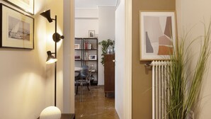Um corredor com quadros nas paredes, luminária de chão, radiador e planta em vaso.