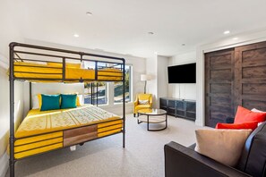 Ein Hotelzimmer mit Etagenbett, einer Couch, einem Sessel, einem Fernseher und einer großen Holztür.