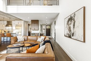 A spacious living area with a large sofa set, a dining table, and a kitchen in the background.
