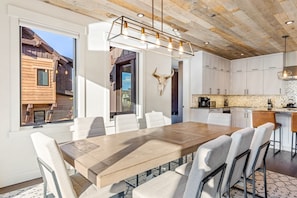 A modern kitchen with a wooden dining table, white chairs, and a kitchen island.