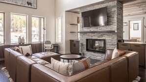 A modern living room with a stone fireplace, leather sectional sofa, and a flat-screen TV mounted on the wall.