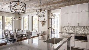 A modern kitchen with a large island, white cabinetry, and geometric pendant lights.