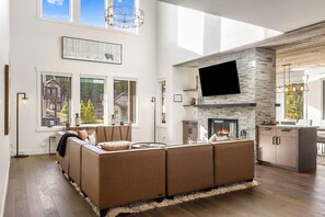 Un salon moderne doté d’un grand canapé d’angle, d’une cheminée et d’un téléviseur à écran plat fixé à un mur en pierre.