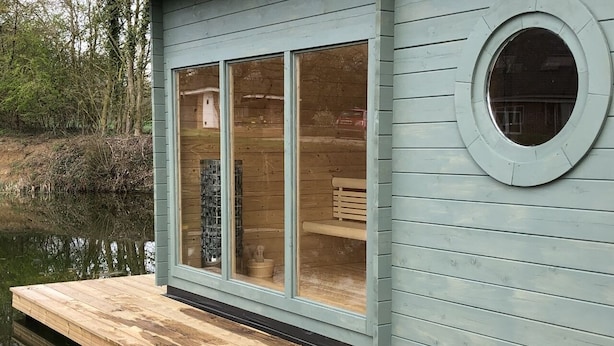 Une jetée en bois s’étendant sur une étendue d’eau calme, avec une cabane dotée de grandes fenêtres et d’une fenêtre circulaire sur le côté droit.