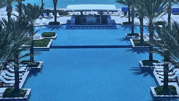Zona de piscina con sillas de descanso y palmeras, con vistas al océano.