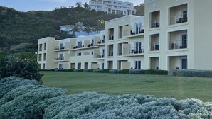 Un hotel de varios pisos con balcones, un césped cuidado y vistas a una colina con otros edificios.
