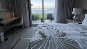 Habitación de hotel con una cama grande, un escritorio, una silla, una lámpara y vista al océano.