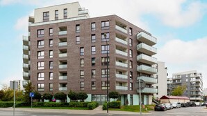 A multi-story residential building with balconies, a pedestrian crossing, and parked cars. - Modern Studio with Balcony | Close to Arkadia Shopping Center (Warszawa)