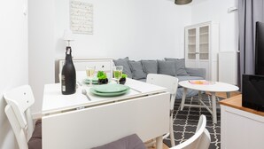 A modern living room with a white sofa, a dining table with green plates, a black lamp, and a white cabinet. - Modern Studio with Balcony | Close to Arkadia Shopping Center (Warszawa)