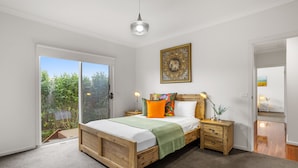 A bedroom with a wooden bed, a sliding glass door to a garden, a bedside table with a lamp, and a wall-mounted artwork. - Tumby on Rye (Rye)