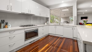 A modern kitchen with white cabinets, a stainless steel range, and a wooden floor. - Tumby on Rye (Rye)