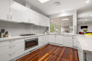 A modern kitchen with white cabinets, a stainless steel range, and a wooden floor. - Tumby on Rye (Rye)