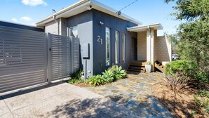 A modern two-story house with a grey exterior, a number 21 sign, a gated driveway, and a stone pathway leading to the entrance. - Tumby on Rye (Rye)