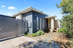 A modern two-story house with a grey exterior, a number 21 sign, a gated driveway, and a stone pathway leading to the entrance. - Tumby on Rye (Rye)