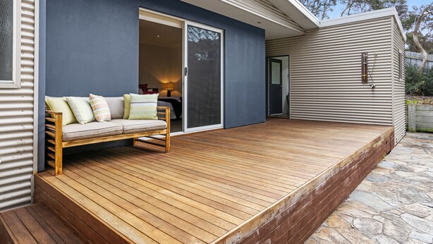 A wooden deck with a sofa and a sliding glass door leading to a room. - Tumby on Rye (Rye)