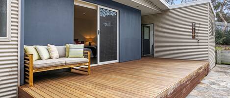 Una terraza de madera con un sofá y una puerta corrediza de vidrio que da a una habitación.