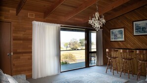 Un intérieur en bois agrémenté d’une grande porte-fenêtre coulissante donnant sur un balcon, d’un lustre et d’un coin bar avec des tabourets.
