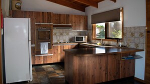 Une cuisine avec des meubles en bois, un four à micro-ondes encastré, un réfrigérateur et une fenêtre donnant sur un espace verdoyant.