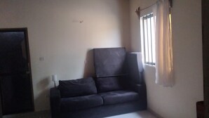 Ein Zimmer mit einem dunkelbraunen Sofa, einer geschlossenen Tür und einem Fenster mit Vorhängen.