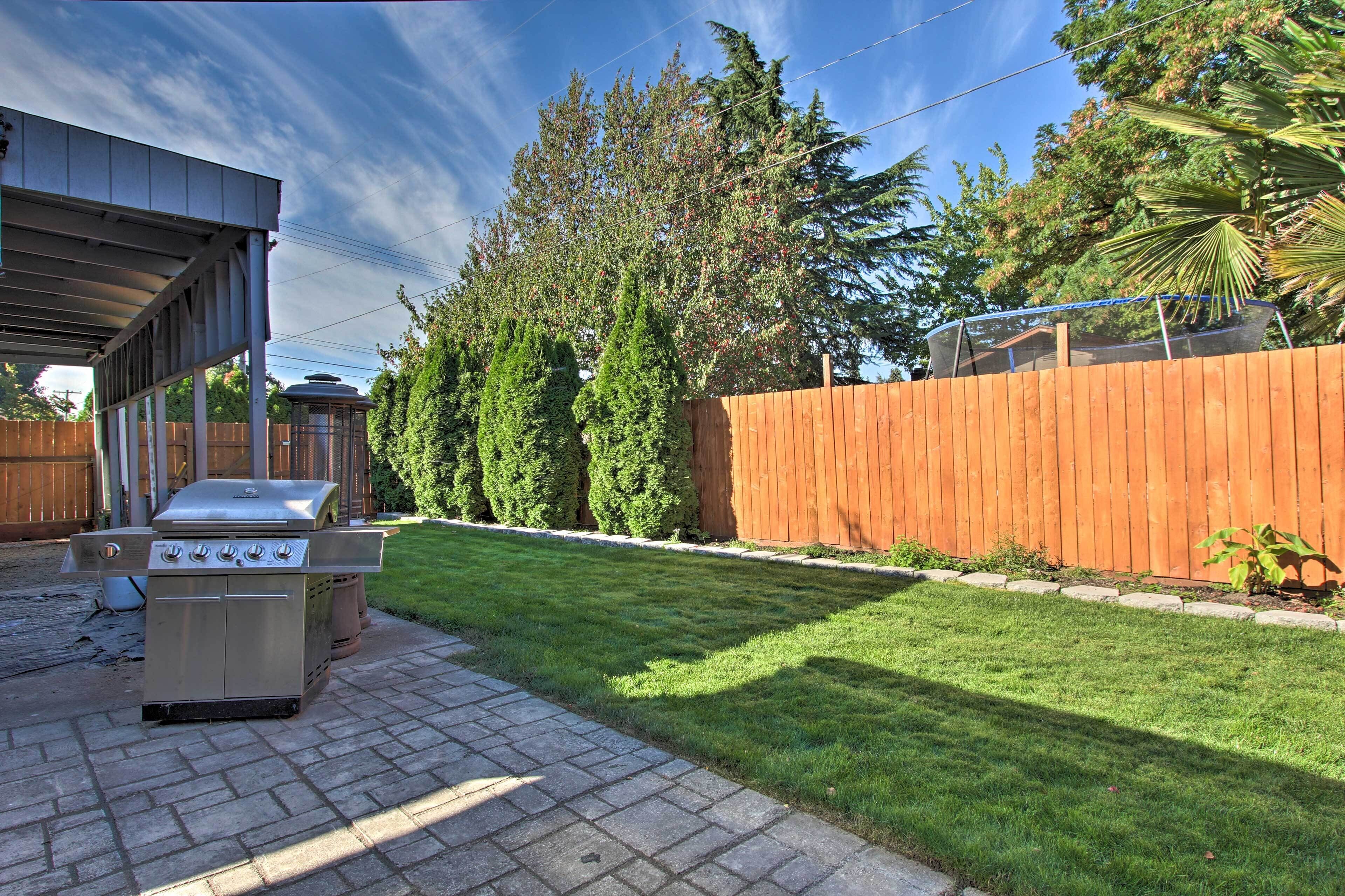 A backyard with a barbecue grill, a wooden fence, and a well-maintained lawn.