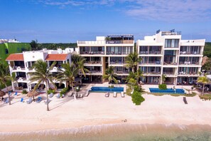 A beachfront hotel with multiple balconies, a pool area, and palm trees.