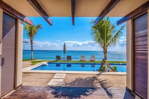 A pool area with a view of the ocean, lounge chairs, and palm trees. - Charming garden view studio with AC, pool and WifFi! (Akumal)