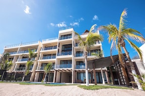 A multi-story hotel with balconies, palm trees, and a pool area.