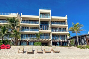 A multi-story hotel with balconies, a beachside location, and a sandy area with lounge chairs. - Charming garden view studio with AC, pool and WifFi! (Akumal)