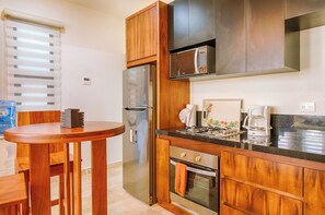 A compact kitchen with wooden cabinets, a stainless steel refrigerator, a built-in oven, and a coffee maker. - Charming garden view studio with AC, pool and WifFi! (Akumal)