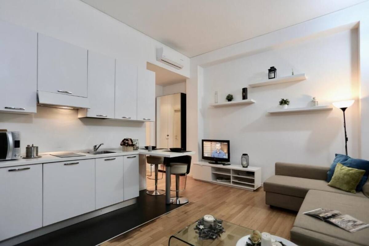 A modern kitchen with white cabinets, a dining area with a table and chairs, a television, and a sofa in a living room.