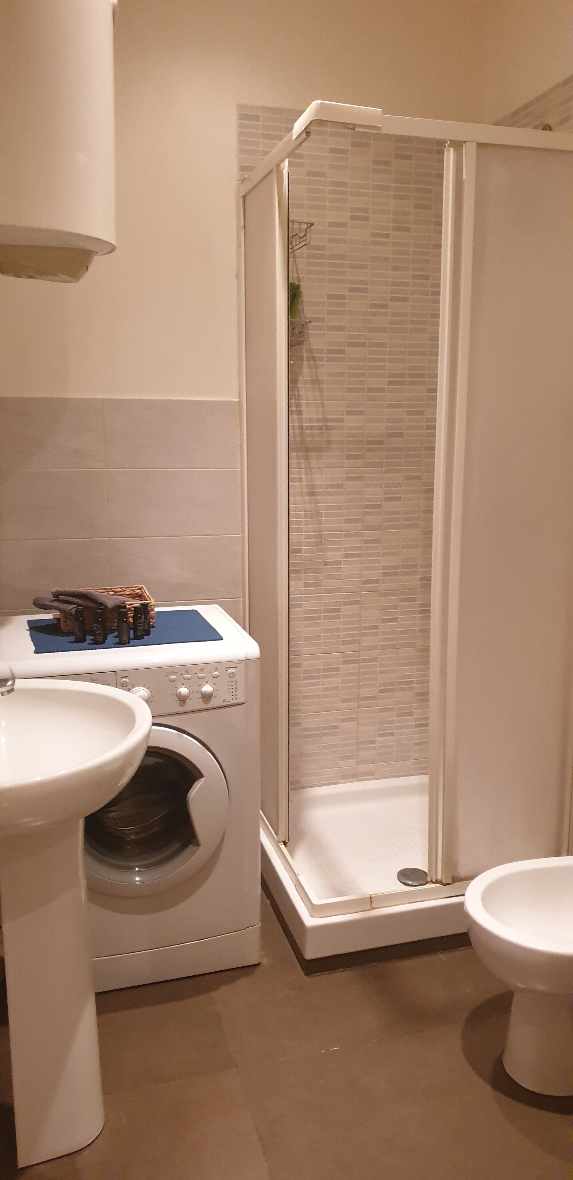 Ett badrum med tvättmaskin, handfat, toalett och en dusch med glasväggar.