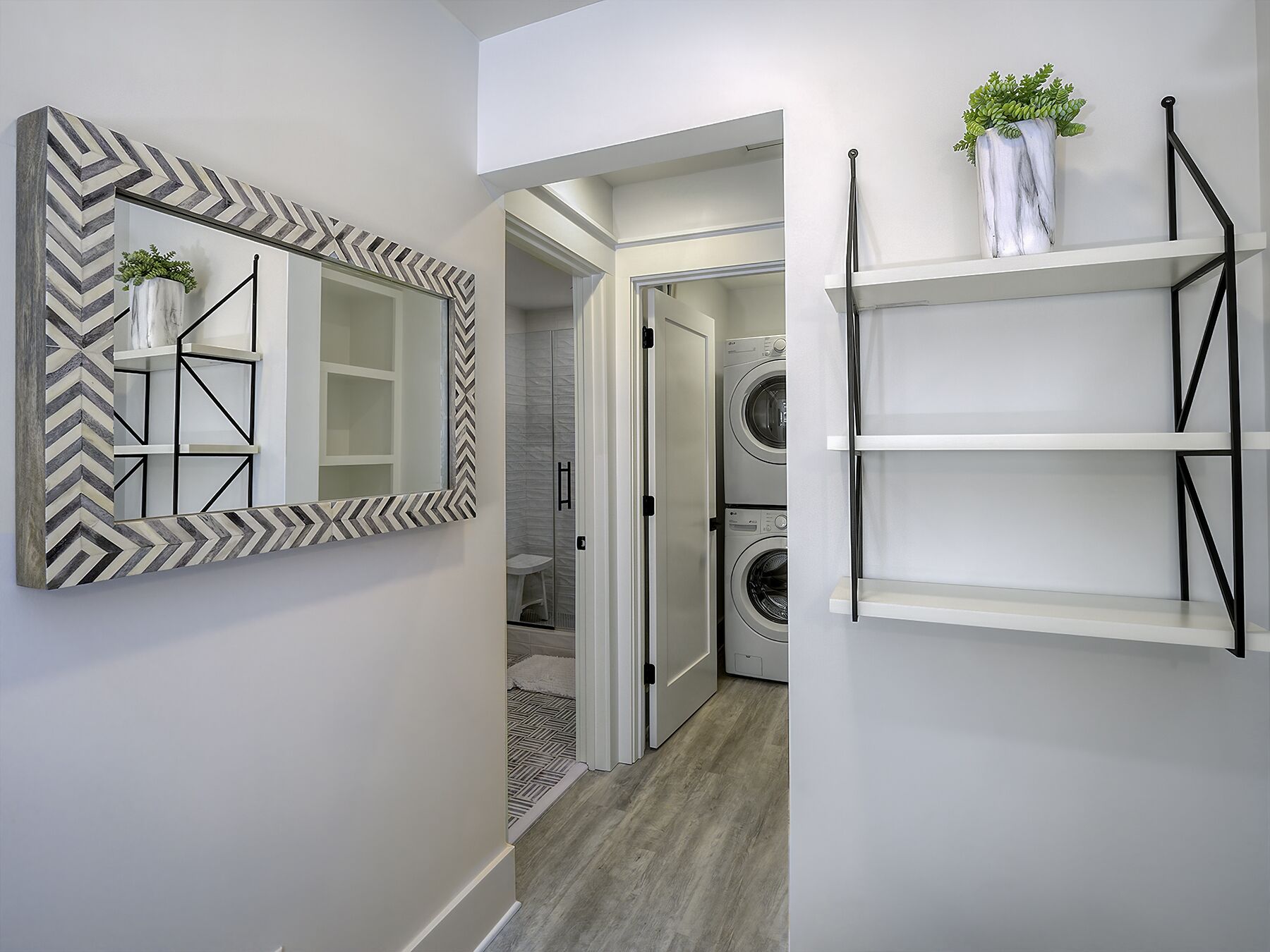 A hallway with a chevron-patterned mirror, a white shelving unit, and a potted plant.