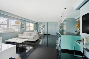 A modern living room with a white sofa, a dining table, and a kitchen area with a bar.