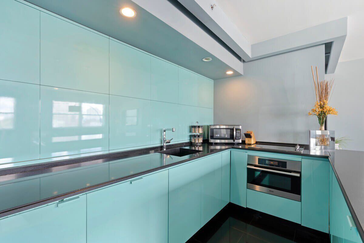 A modern kitchen with teal cabinetry, stainless steel appliances, and a black countertop.
