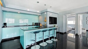 A modern kitchen with a central island, bar stools, and a flat-screen TV.