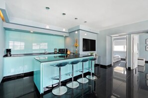 A modern kitchen with a central island, bar stools, and a flat-screen TV.